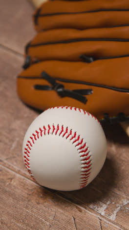 Vídeo-Vertical-De-Cerca-De-La-Naturaleza-Muerta-Del-Estudio-De-Béisbol-Con-Pelota-Y-Guante-De-Receptor-En-El-Suelo-De-Madera